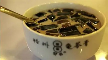 A bowl of Wuzhou guilinggao cubes served with milk, in a white bowl printed with the Shuangqian brand name
