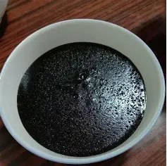 A home-style bowl of dark herbal jelly in a plain white bowl, on a wooden table